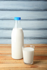 Bottle of tasty milk with glass on wooden table