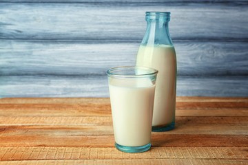 Glass of tasty milk with bottle on wooden table