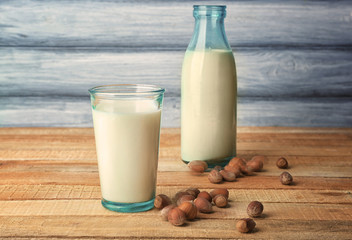 Glass of tasty hazelnut milk with bottle on wooden table