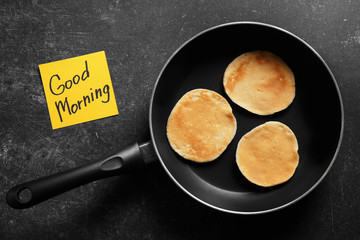 Three pancakes in frying pan and note GOOD MORNING on black background