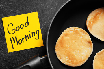 Three pancakes in frying pan and note GOOD MORNING on black background closeup