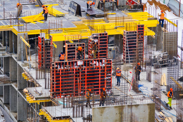 Construction site with a bright yellow formwork and builders in bright multi-colored construction...