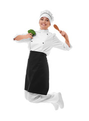 Young woman chef with broccoli and wooden spoon in hands jumping on white background