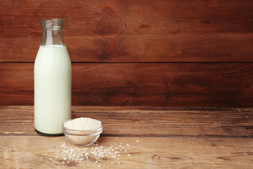Bottle of milk and little bowl with rice on wooden background