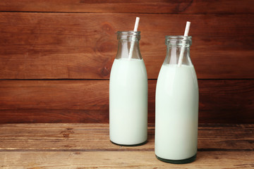 Two bottles of milk with straws on wooden background