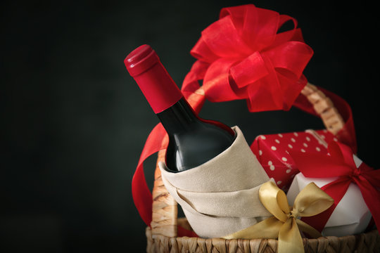 Wine bottle with gift boxes in wicker basket on dark background