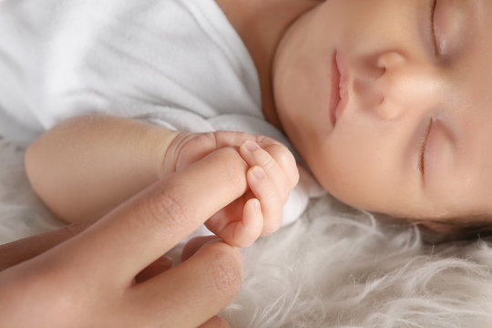Cute little baby holding mother's finger while sleeping, closeup