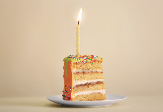 Slice of birthday cake with candle on color background