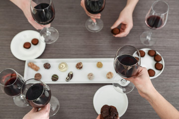 Female hands holding glasses of red wine and sweets over wooden table