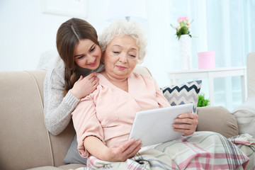 Beautiful girl with grandmother using tablet at home