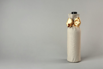 St. Valentine's Day concept. Wine bottle in gift linen pouch with satin ribbon on light background