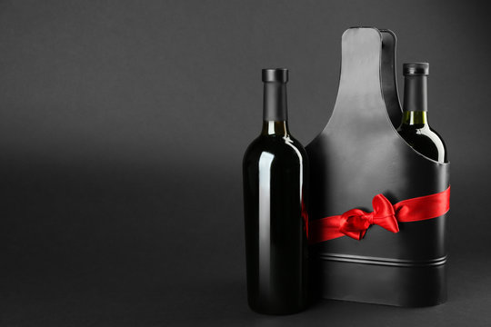 St. Valentine's Day concept. Two wine bottles and black metal gift box with satin ribbon on dark background