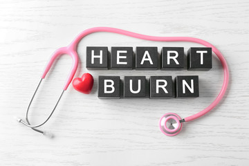 Text HEART BURN made of cubes and stethoscope on wooden background
