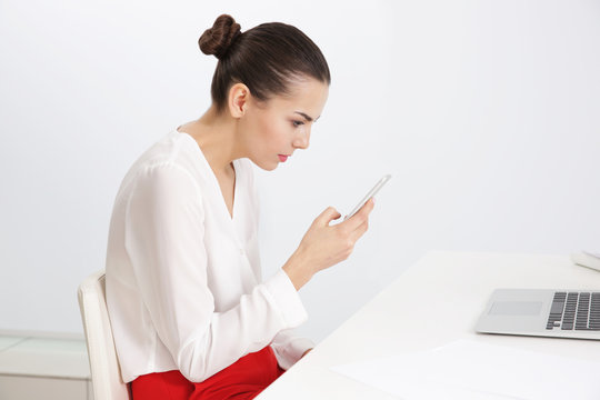 Incorrect posture concept. Young woman with phone sitting at table indoors