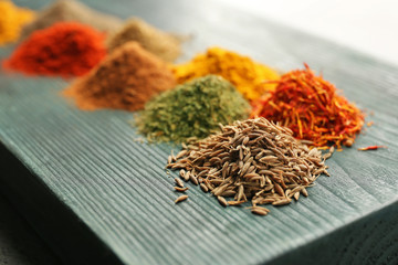 Wooden board with heaps of various spices, closeup