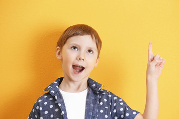 Cute little boy with index finger up on color background