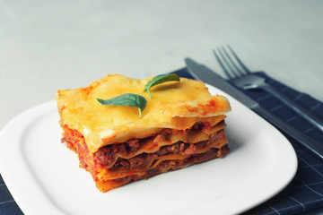 Plate with delicious lasagna and black napkin on table
