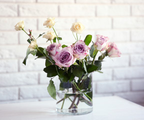 Glass vase with bouquet of beautiful flowers on brick wall background
