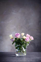 Glass vase with bouquet of beautiful roses on color background