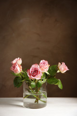 Glass vase with bouquet of beautiful roses on color background