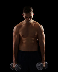 Fototapeta na wymiar Sporty man doing exercises with dumbbells on black background
