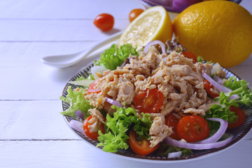 tuna fish salad with lettuce, onion, lemon and tomatoes on white wooden table in background.