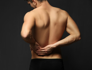 Young man suffering from backache on dark background