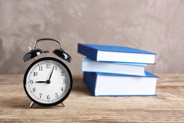 Alarm clock and stack of books on wooden table