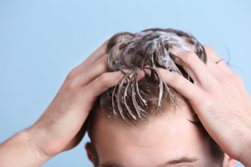 Young man washing hair on color background, closeup