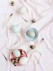 White and green Easter eggs, quail eggs and feathers on pink textile background. Flat lay, top view. Traditional spring concept. Easter concept.