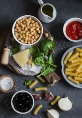 Ingredients for cooking rigatoni pasta with chickpeas, spinach and olives in a tomato sauce on a dark background, top view. Vegetarian food concept