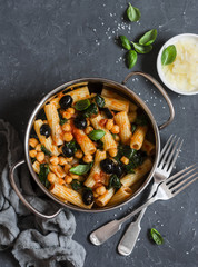 Rigatoni pasta with chickpeas, spinach and olives in a tomato sauce on a dark background, top view. Vegetarian food concept