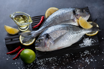 Black wooden cutting board with a couple of raw fresh sea breams