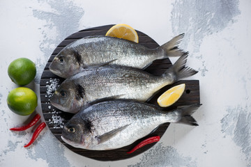 Raw sea breams with seasonings on a white concrete background