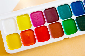 Palette of watercolor paints, brushes and paper for a water color on white background, close up.  Selective focus