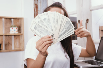 Happy woman thumbs up and holding money while working on laptop.