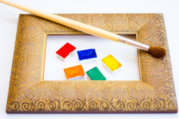 Naklejka premium The palette of watercolor paints and brush and frame on a white background, closeup. Selective focus. Place for an inscription