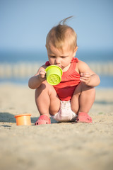 Baby playing on the sandy beach near the sea. Cute little girl in red dress with sand on tropical beach. Ocean coast.
