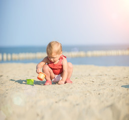 Baby playing on the sandy beach near the sea. Cute little girl in red dress with sand on tropical beach. Ocean coast.