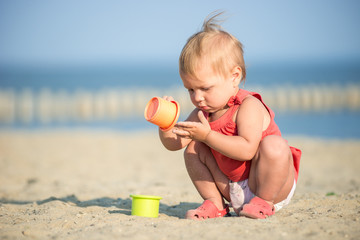 Baby playing on the sandy beach near the sea. Cute little girl in red dress with sand on tropical beach. Ocean coast.