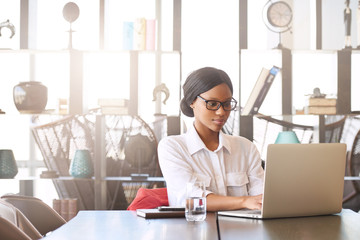 Professional black entrepreneur and businesswoman busy working on her laptop computer while seated at the head of the conference table in the business lounge.