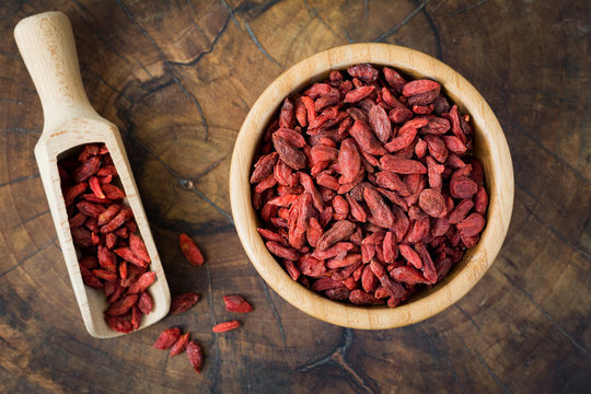 Dried goji berries in a wooden bowl over wooden background. Closeup, top view, horizontal image