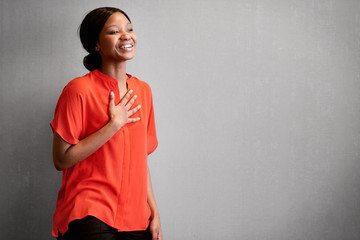 Black female business person busy laughing with one hand against her chest while wearing a bright colourful orange blouse with space for copy text on the right of the image. - obrazy, fototapety, plakaty