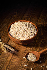 oat flakes in a wooden bowl on a wooden background near the ears of wheat. Wooden spoon with flakes