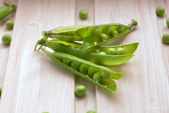 Open, fresh pea pods and peas on wooden background close up