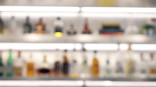 Blurred liquor bottles on backlit bar shelves. Variety or choice concepts. 4K background bokeh pan shot
