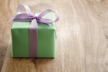 green paper gift box with purple ribbon bow on old wood table, with copy space