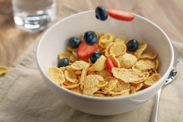 berries falling into corn flakes for breakfast in bowl on table, breakfast preparation