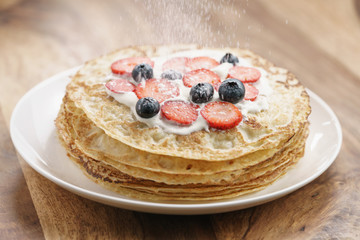 sugar powder fall on fresh blinis or crepes with fresh berries and cream, sweet food