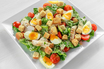 Fresh healthy Caesar salad with chicken, eggs, tomatoes, Cheese and Croutons on white plate